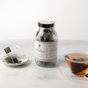 Jar of tea bags with a teacup and loose tea on a white background